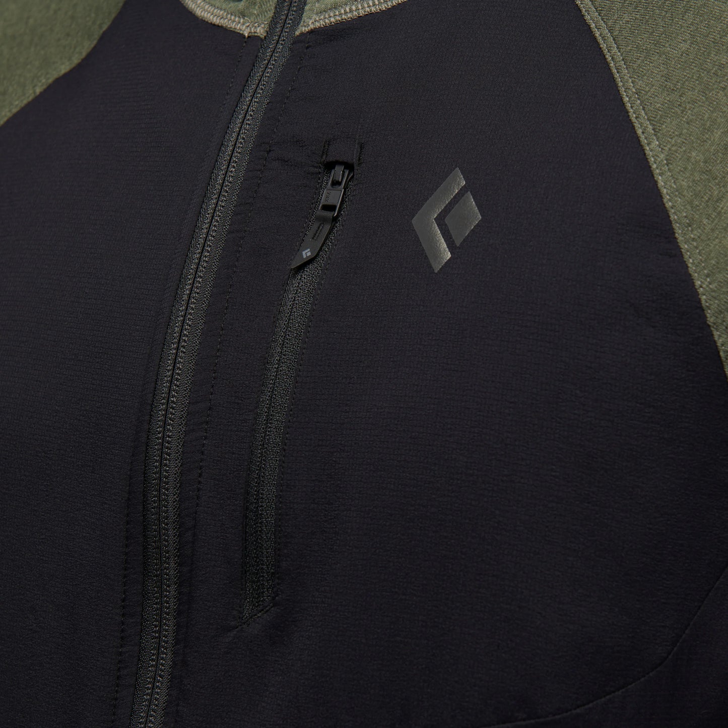 Close-up of a black jacket with a zipper and brand logo on a green background