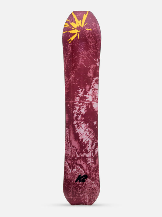 A single snowboard shown upright against a light gray studio background. The board has a dark burgundy base with a distressed white pattern and a yellow graphic near the nose, plus a small black logo near the tail.