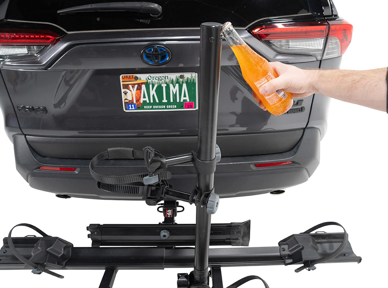 Person using a bottle to clean a bike rack attached to a car, with a Yakima license plate on the car.