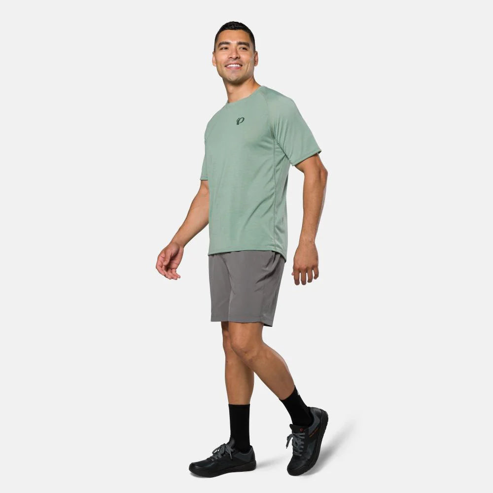 Man wearing a green t-shirt and gray shorts on a white background