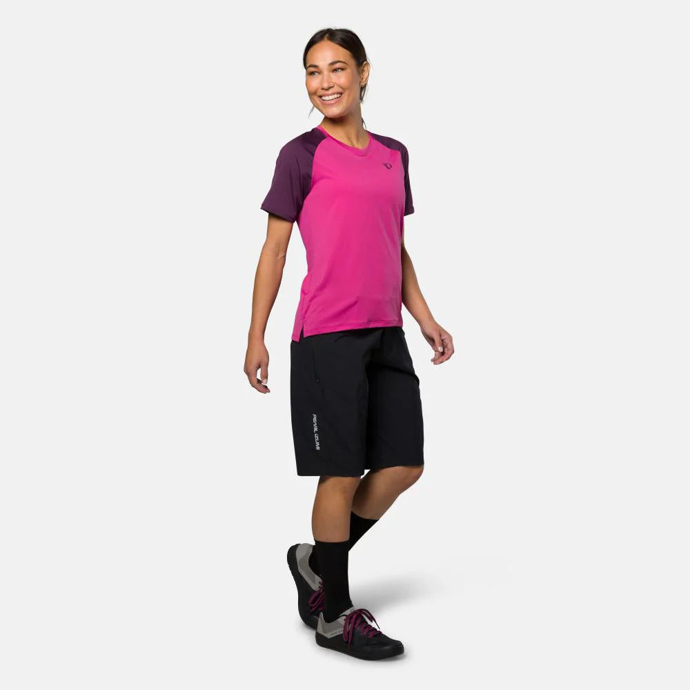 Woman wearing a pink and purple athletic shirt with black shorts on a white background