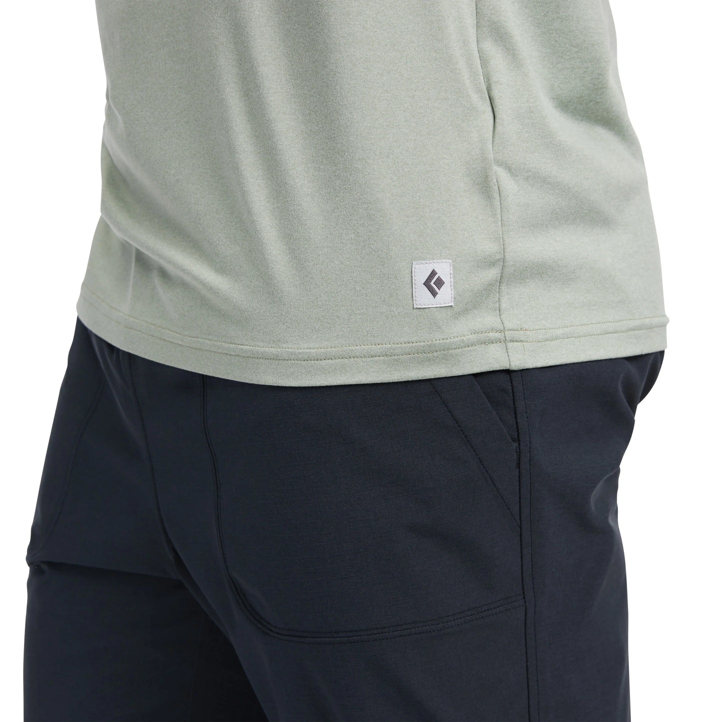 Close-up of a person wearing a light gray shirt with a logo and dark blue pants on a white background.