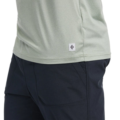 Close-up of a person wearing a light gray shirt with a logo and dark blue pants on a white background.