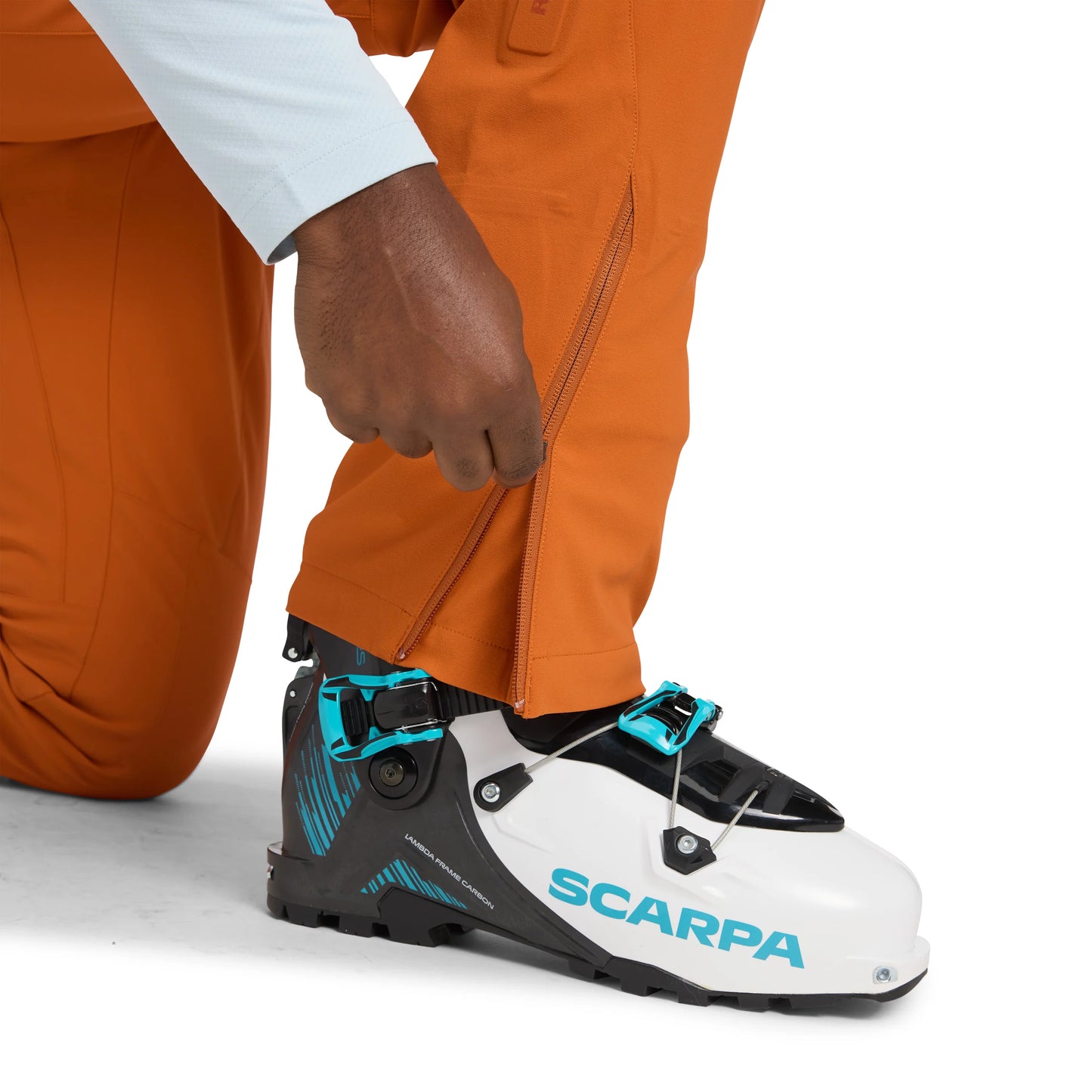 Person wearing orange pants and a white shirt, adjusting a black and white ski boot with blue accents on a white background.