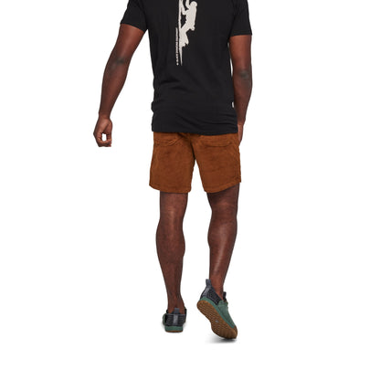 Person wearing a black t-shirt with a white graphic and brown shorts on a white background