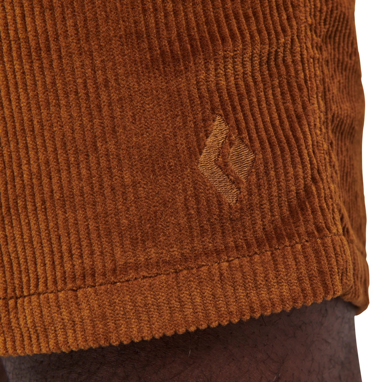 Close-up of brown corduroy fabric with a small logo on a plain background