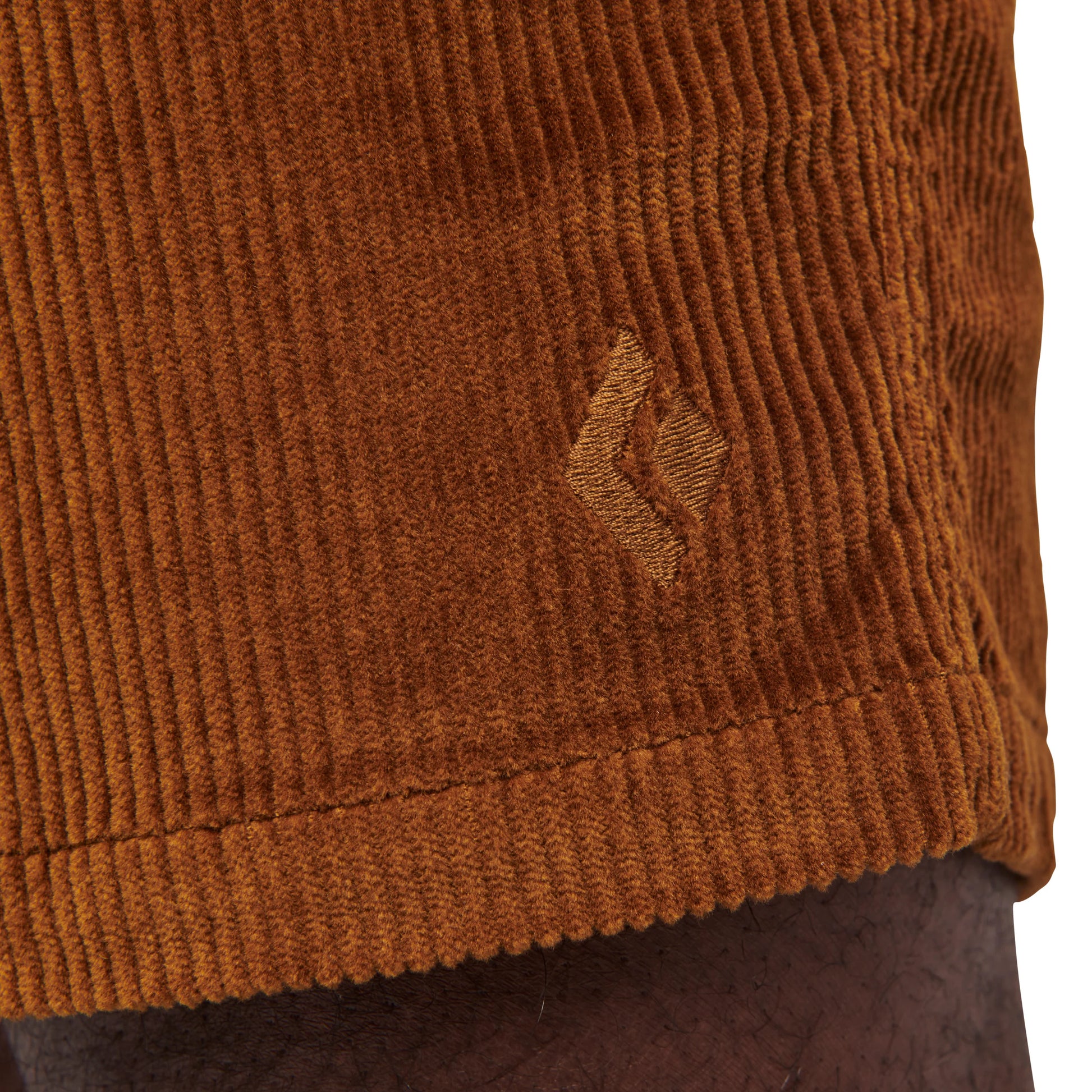 Close-up of brown corduroy fabric with a small logo on a plain background