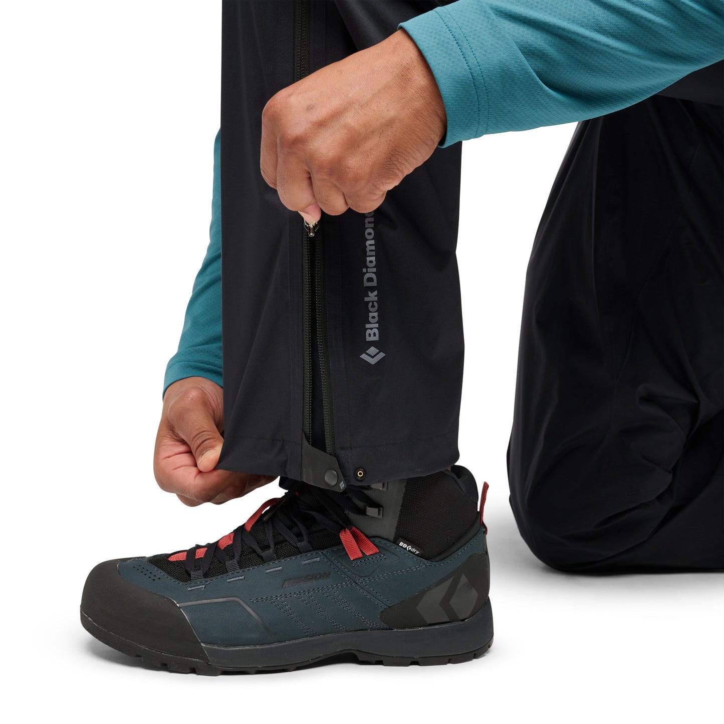 Person wearing black hiking pants with a visible brand logo, adjusting a shoe.