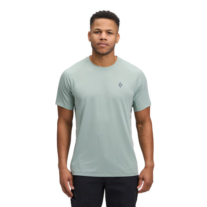 Man wearing a light green t-shirt with a small logo on a white background