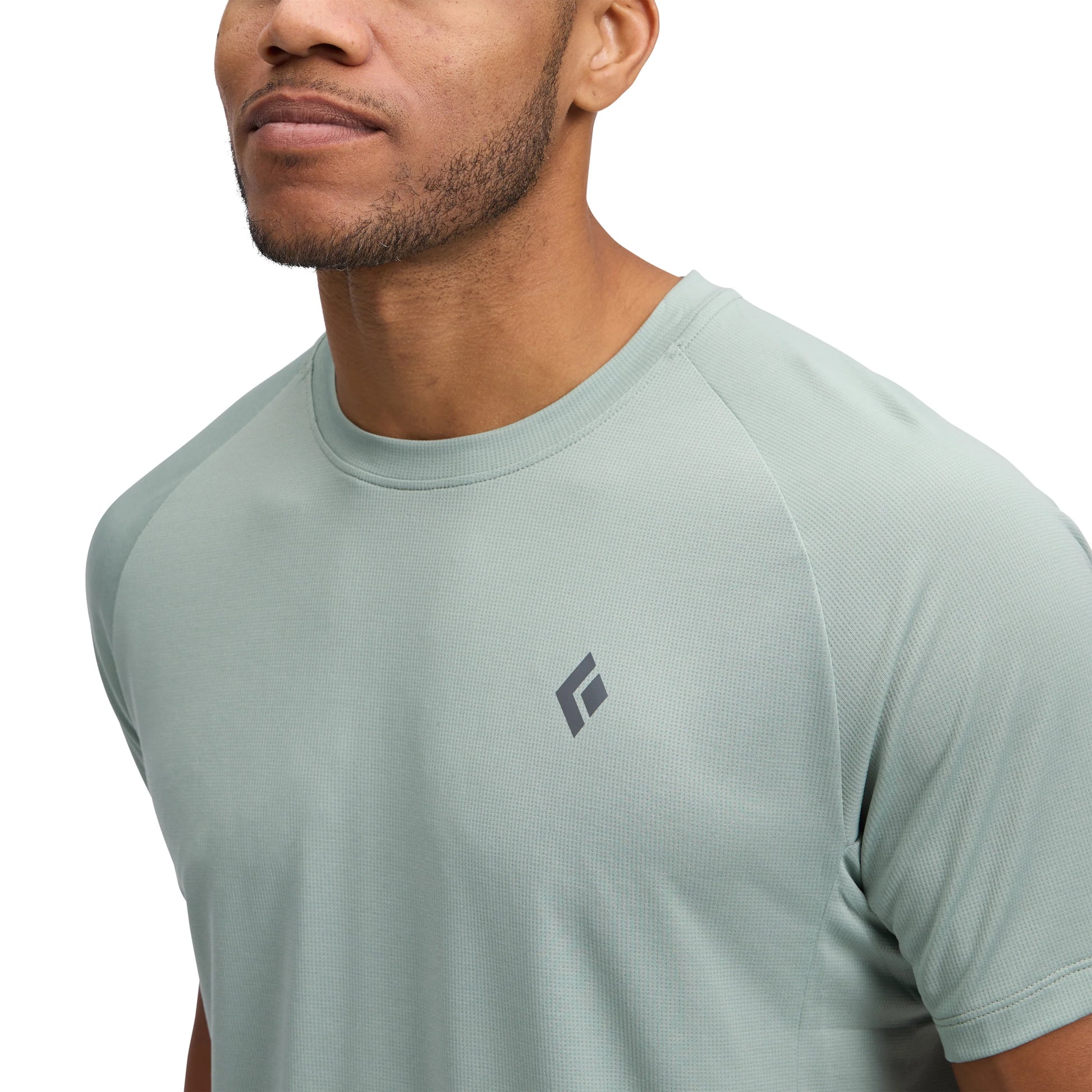 Man wearing a light green t-shirt with a brand logo on a white background