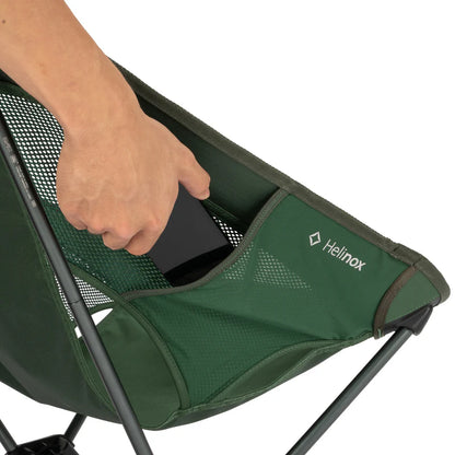 Green camping chair with a hand reaching into it, featuring the Helinox logo.