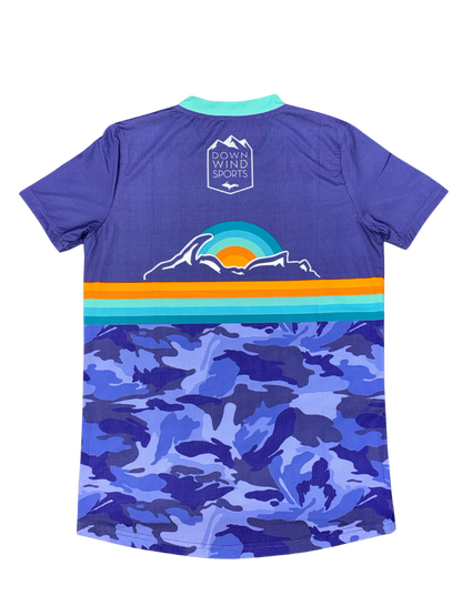 The back of a purple short-sleeve athletic jersey with a blue camouflage pattern on the lower half, a horizontal stripe design in orange, teal, and blue across the center, a mountain graphic with a sunset, and a 'Down Wind Sports' logo printed on the upper back.