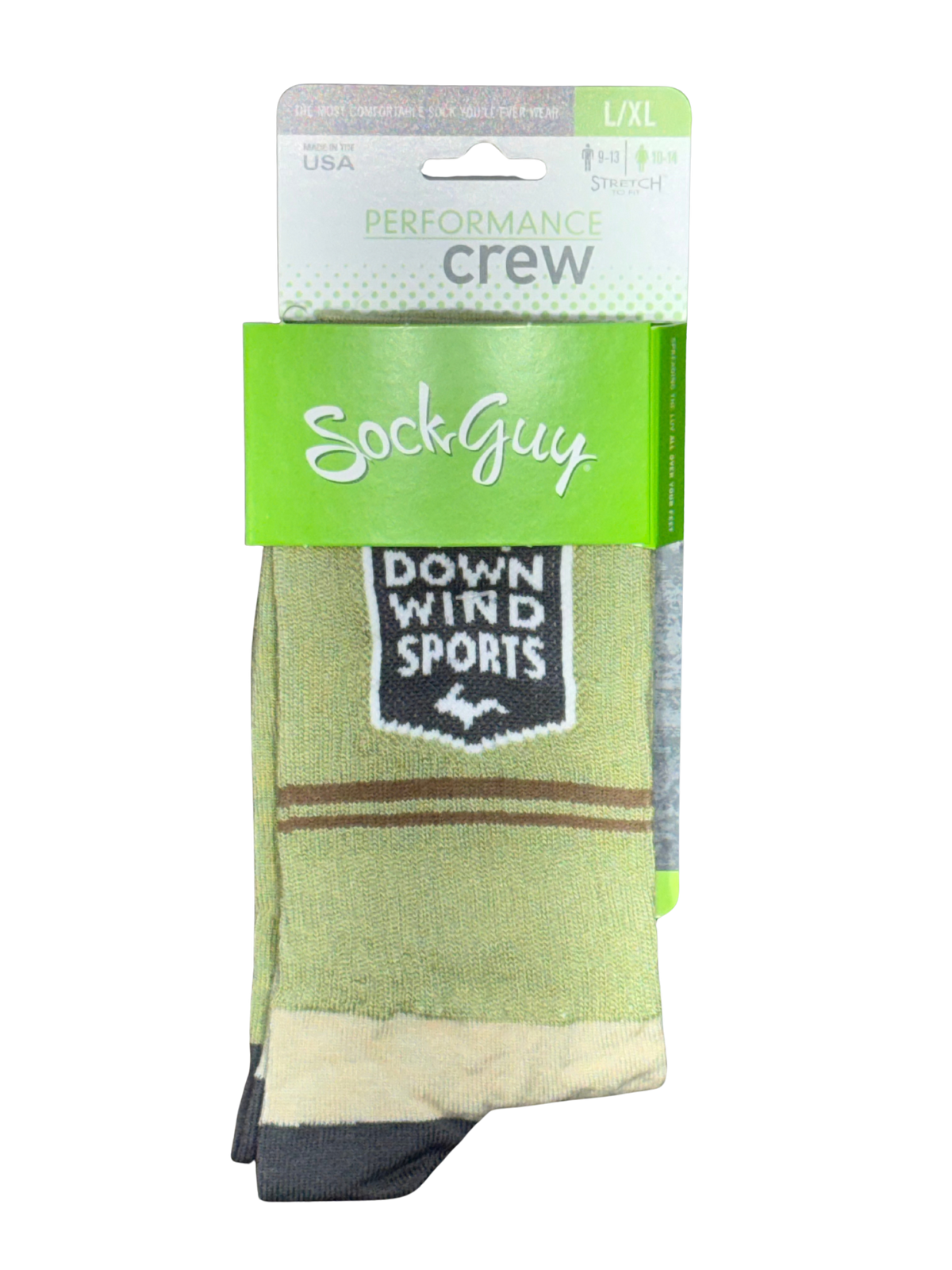 A pair of SockGuy crew socks in a light olive green colorway, featuring a black and white 'Down Wind Sports' shield patch on the side, with brown stripes and a beige cuff. The socks are shown in their retail packaging against a white background.