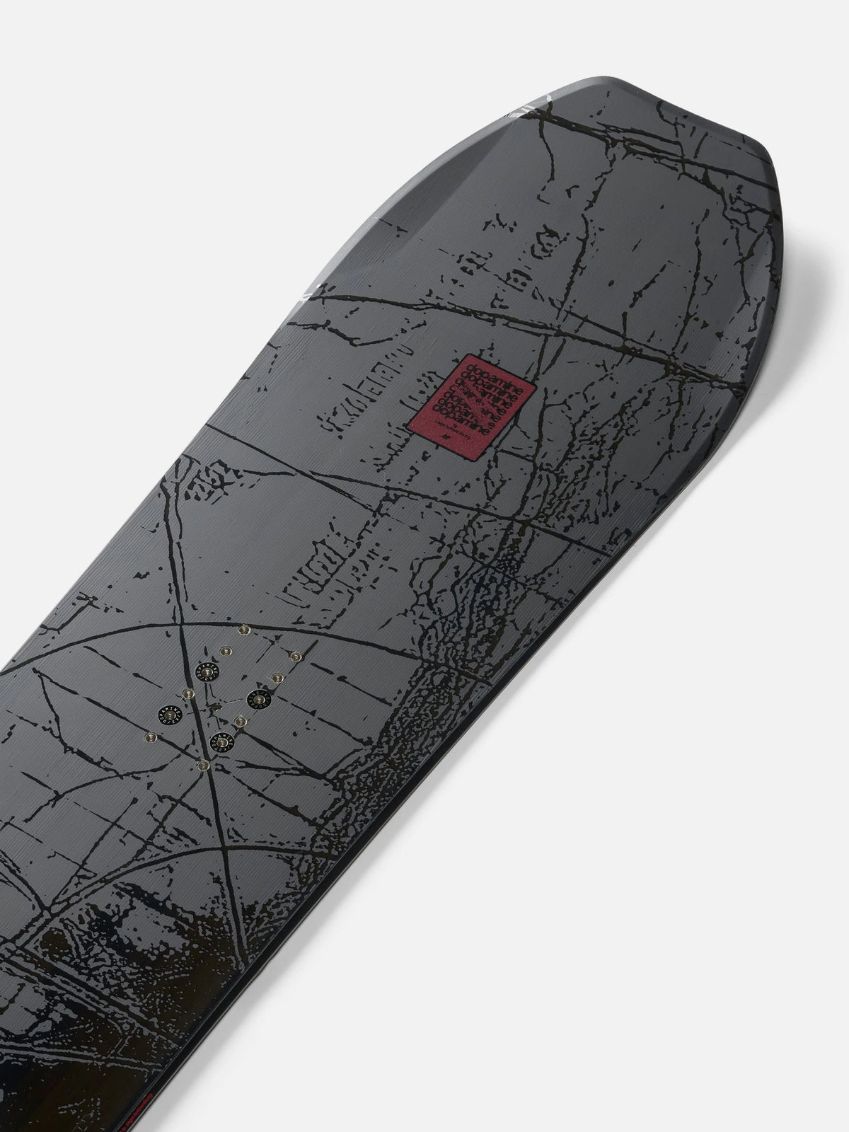 A close-up of a snowboard deck featuring a dark gray and black topographic map design with a small red square logo near the center, photographed on a light gray background.