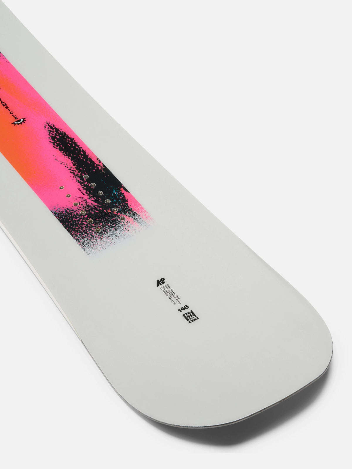 A close-up of a snowboard base showing a white background with a vibrant pink and orange graphic transitioning into a black brushstroke design. Small black technical markings are visible near the tail.