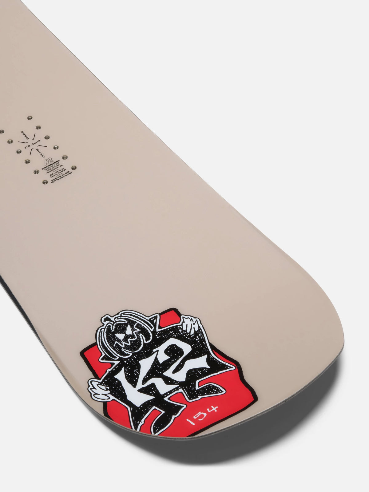 A close-up of a beige snowboard tail showing the K2 brand logo sticker in red, black, and white, on a light gray background.