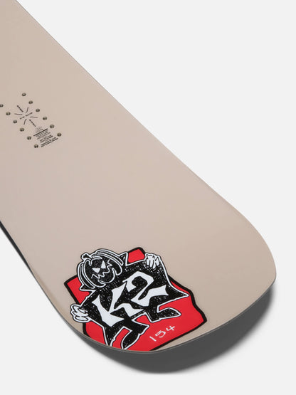 A close-up of a beige snowboard tail showing the K2 brand logo sticker in red, black, and white, on a light gray background.
