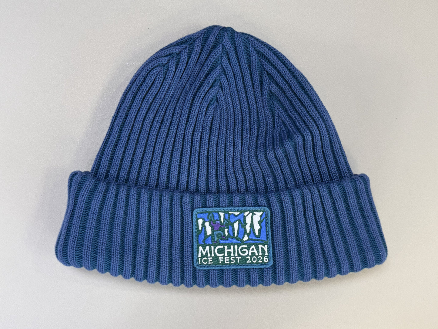 Blue knit beanie with 'Michigan Ice Fest 2026' logo on a light gray background