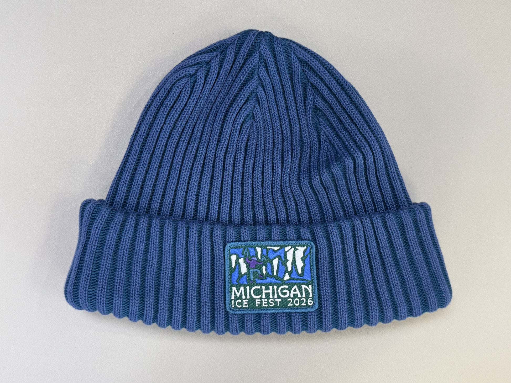 Blue knit beanie with 'Michigan Ice Fest 2026' logo on a light gray background