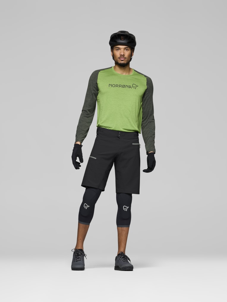 Person wearing a green and gray long-sleeve shirt with black shorts on a gray background