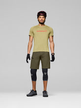 Load image into Gallery viewer, Man wearing a green t-shirt with a brand logo, green shorts, black knee pads, and a helmet on a gray background
