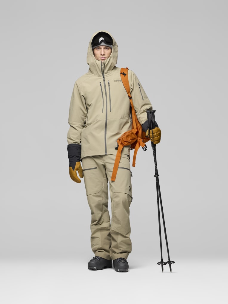 Person wearing a beige ski suit with ski poles and backpack on a gray background