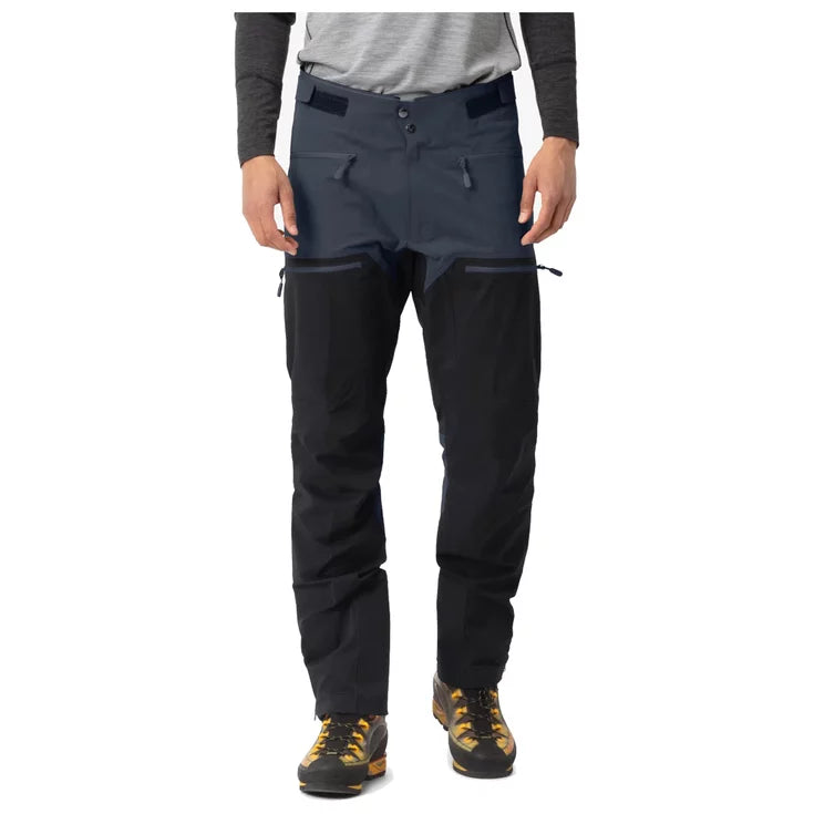 Person wearing dark gray pants with black zippers on a white background