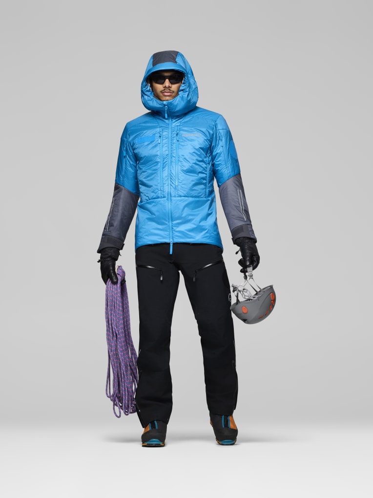 Person wearing a blue jacket with black sleeves and pants, holding climbing equipment on a gray background