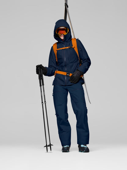 Person wearing a blue ski suit with a backpack and ski poles on a gray background