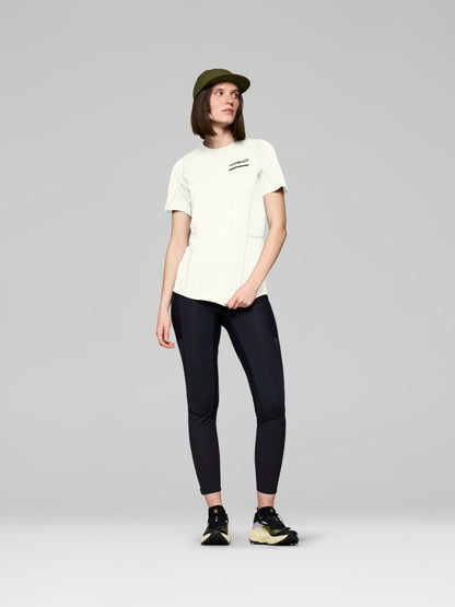 Person wearing a white t-shirt, black leggings, and a green cap on a gray background