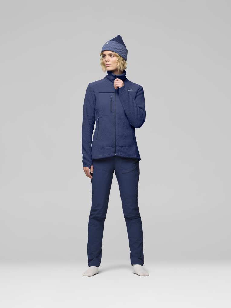 Person wearing a blue jacket and pants with a matching beanie on a gray background