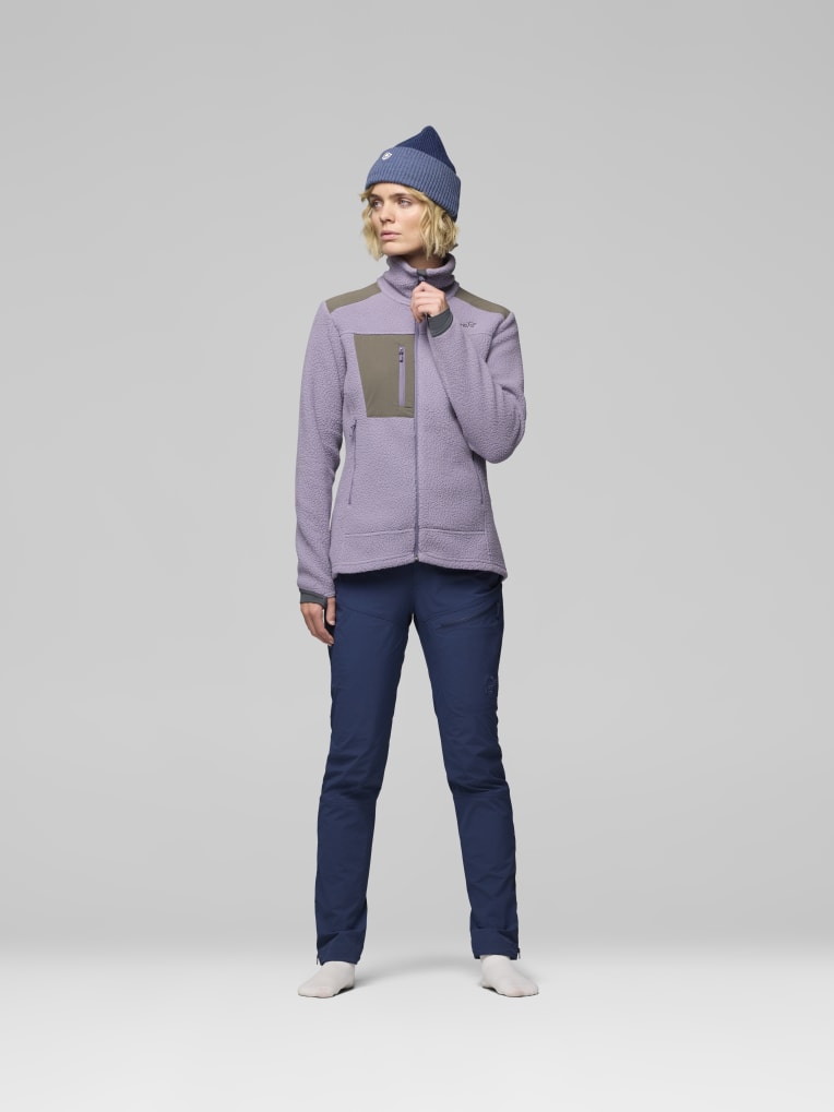 Person wearing a purple jacket and blue pants with a matching beanie on a light gray background