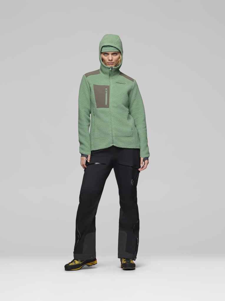 Person wearing a green jacket and black pants on a gray background