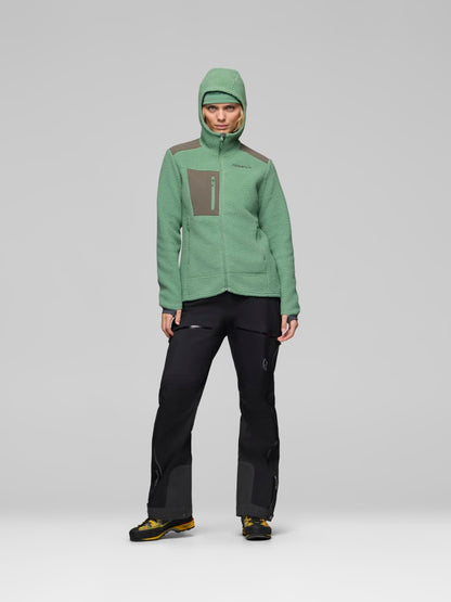 Person wearing a green jacket and black pants on a gray background