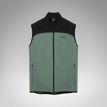 A sleeveless zip-front vest with a black upper yoke, collar, and hem, and a muted sage green lower body. The vest has a small Oakley logo on the left chest and zippered side pockets, shown on a light gray gradient background.