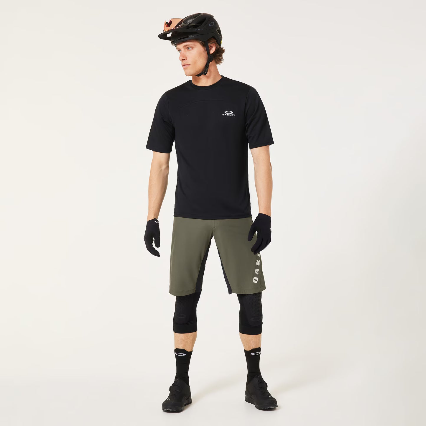 Man wearing a black t-shirt, green shorts, and cycling gear on a white background