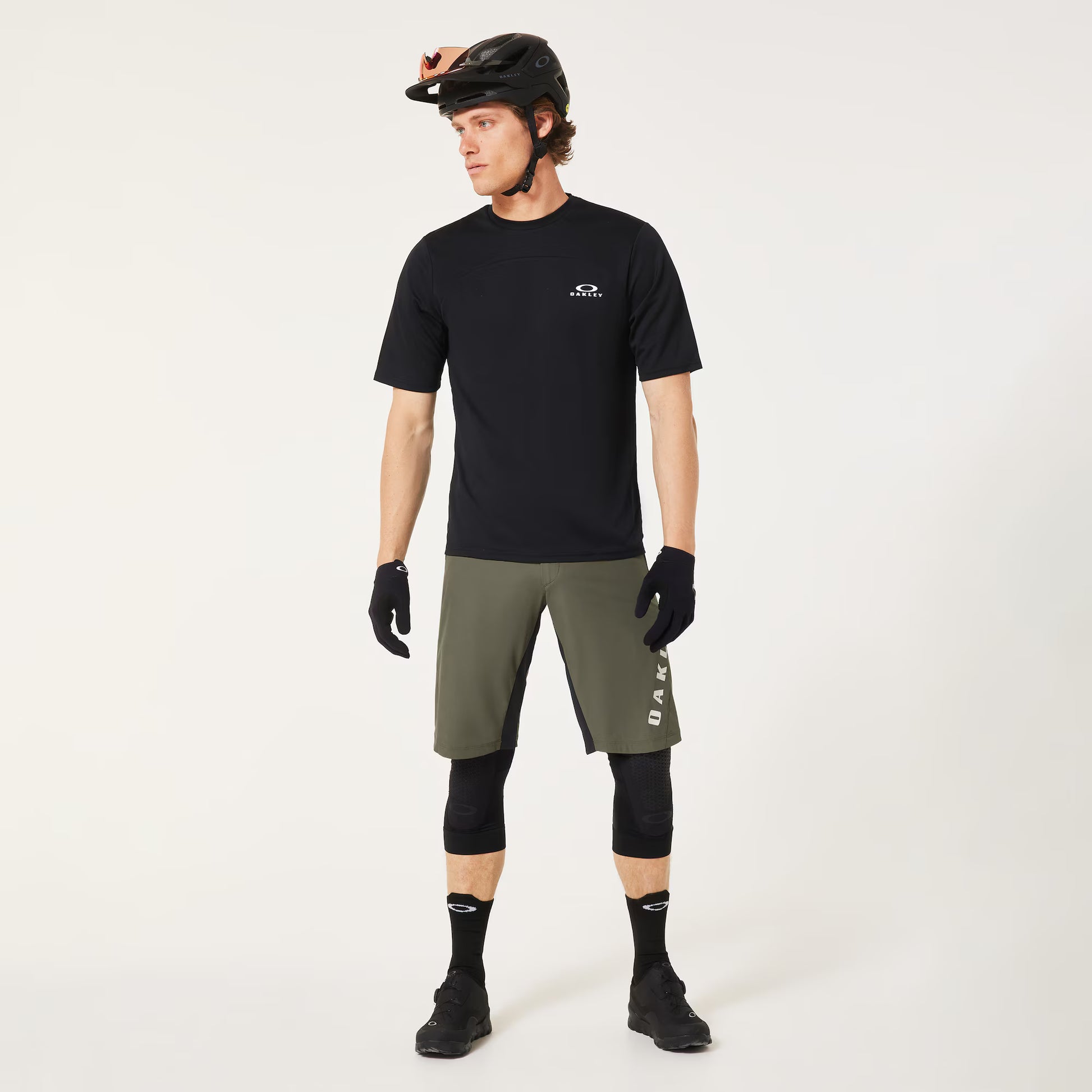 Man wearing a black t-shirt, green shorts, and cycling gear on a white background