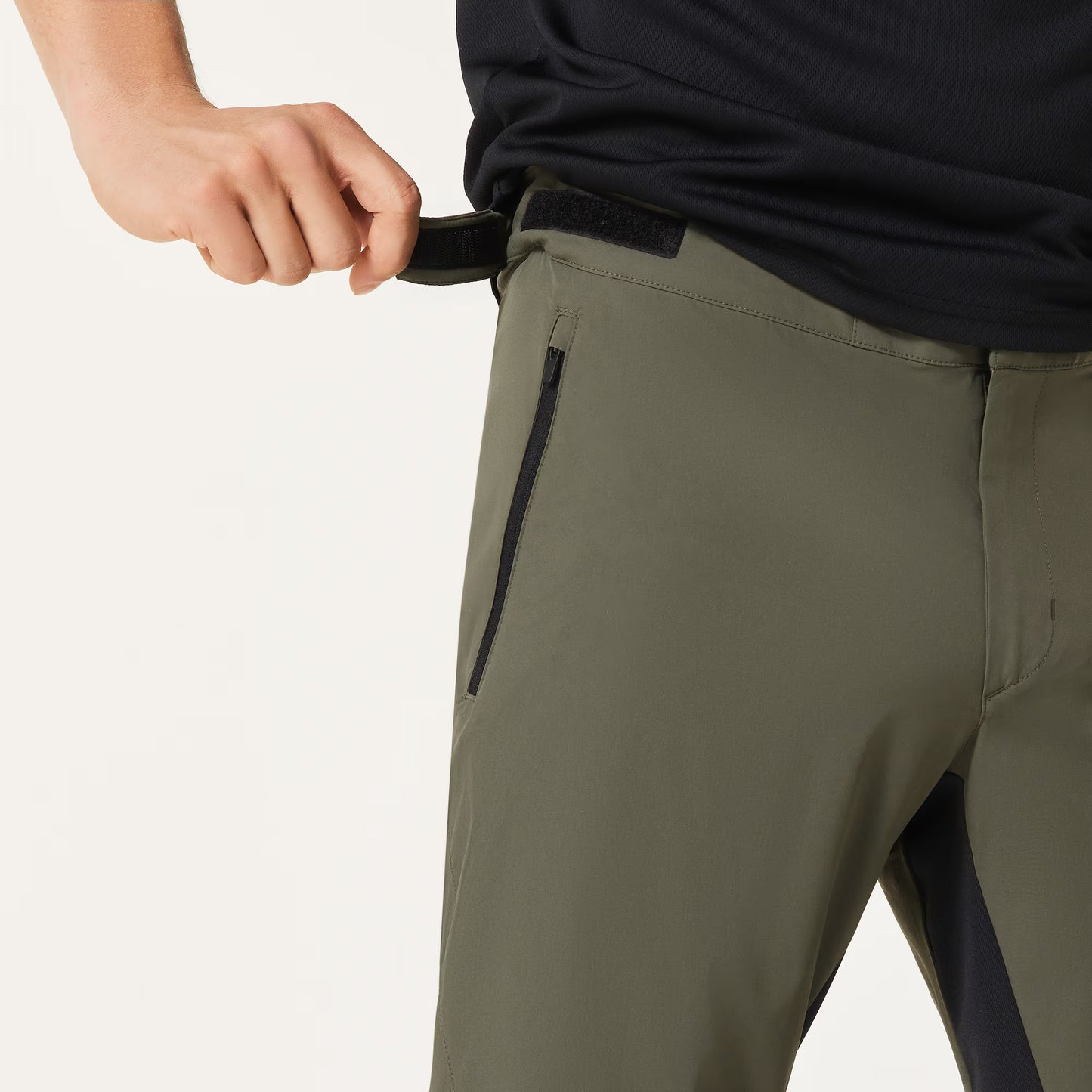 Person wearing olive green pants with black zippers on a light gray background