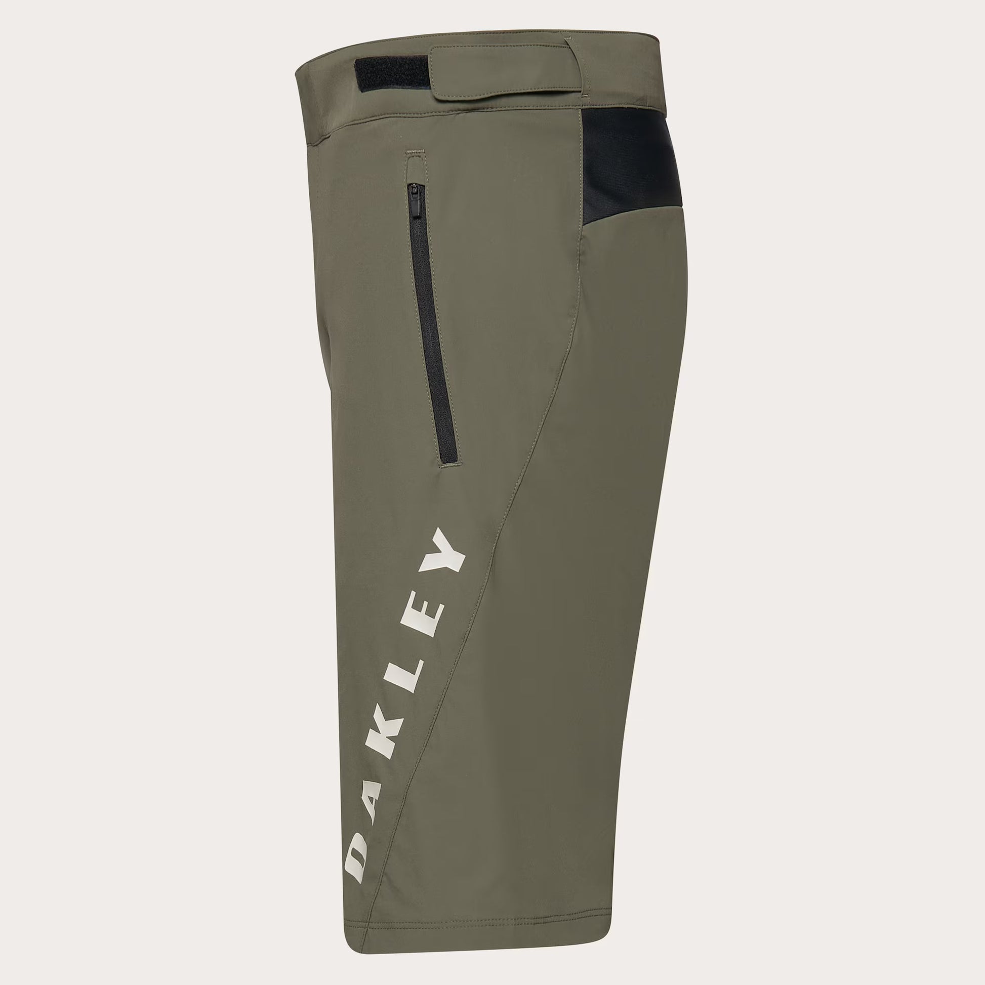 Olive green Oakley cycling shorts with a vertical white 'OAKLEY' logo on the left leg, a black zippered pocket, and a black side panel near the hip, shown against a light gray background.