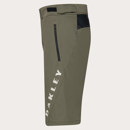 Olive green Oakley cycling shorts with a vertical white 'OAKLEY' logo on the left leg, a black zippered pocket, and a black side panel near the hip, shown against a light gray background.