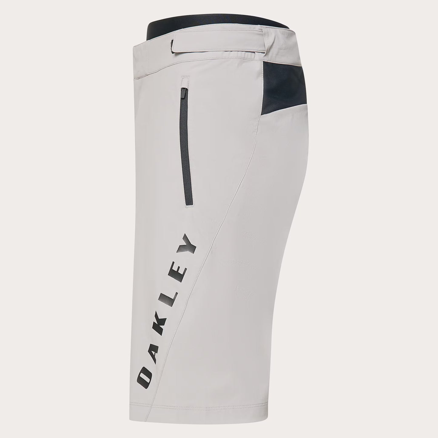 Oakley athletic shorts in light gray with a dark navy waistband, a vertical zip pocket on the left leg, a side pocket with a dark navy accent, and the Oakley logo printed vertically in dark gray on the lower left leg.