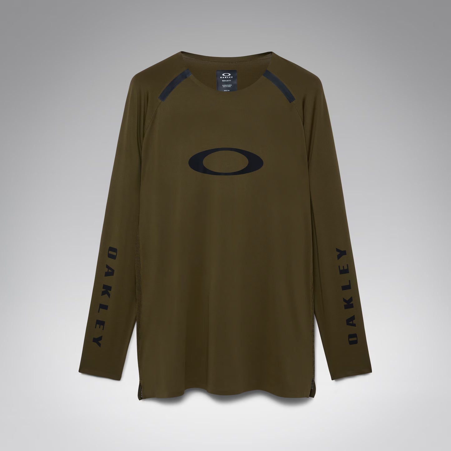 An olive brown long-sleeve athletic shirt by Oakley, featuring a large black Oakley logo on the chest, black vertical branding on both sleeves, and black shoulder detailing, shown against a neutral gray background.
