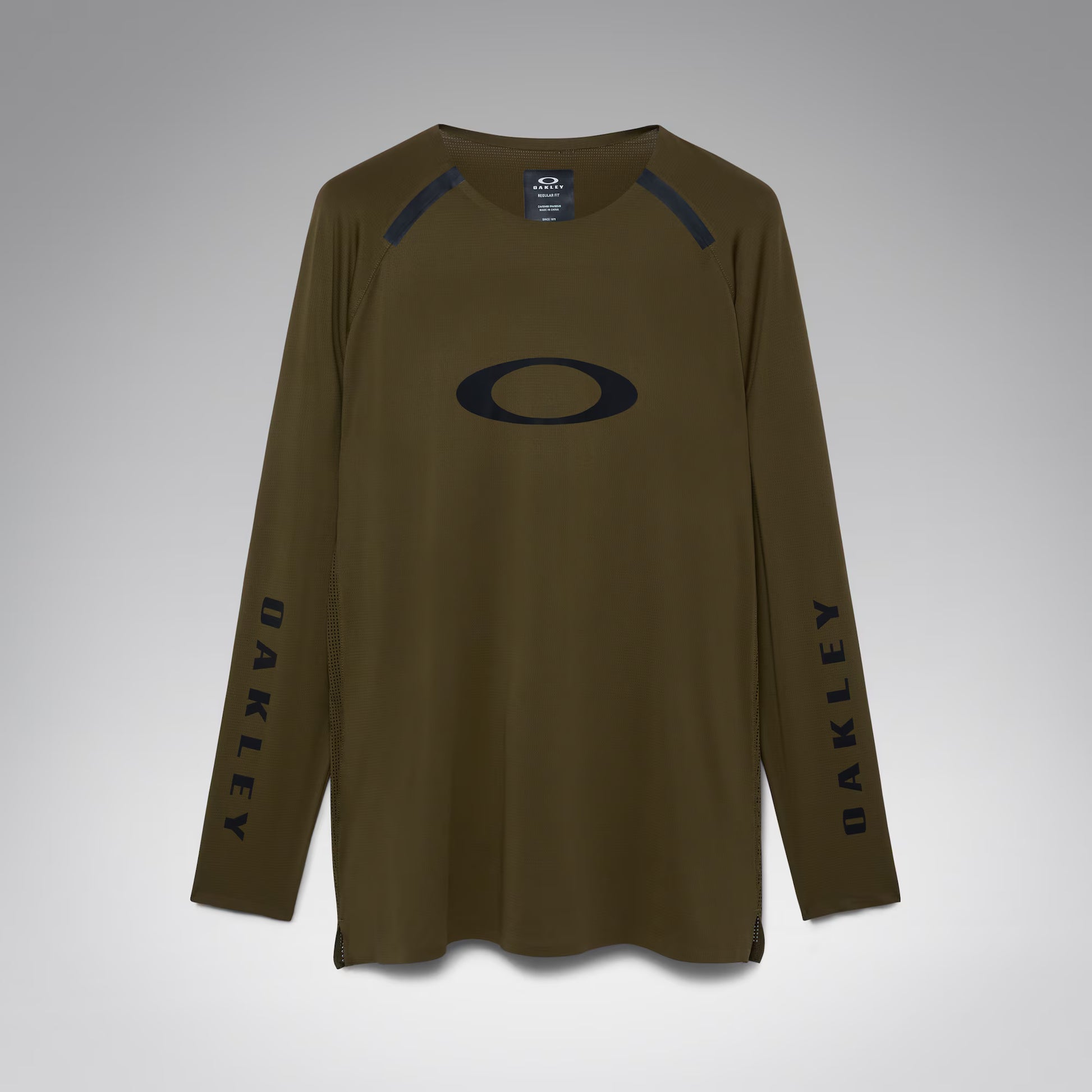 An olive brown long-sleeve athletic shirt by Oakley, featuring a large black Oakley logo on the chest, black vertical branding on both sleeves, and black shoulder detailing, shown against a neutral gray background.
