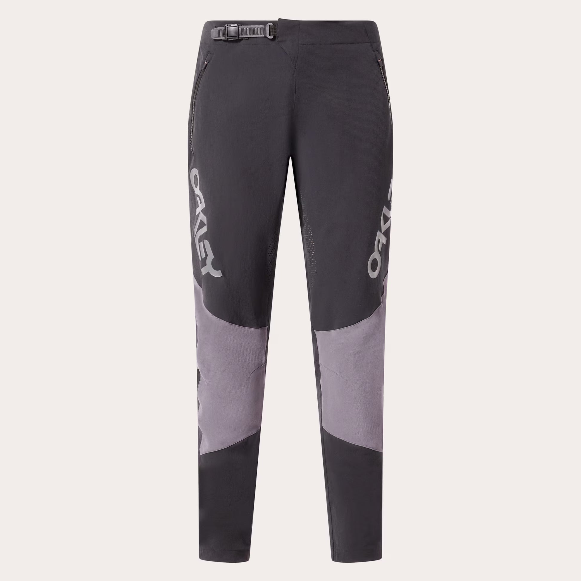 A pair of dark gray and light gray colorblock mountain biking pants with white OAKLEY branding printed vertically on the sides, shown against a light gray background.