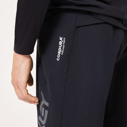 Close-up of a person wearing black Cordura athletic pants, showing the side pocket with white CORDURA branding and part of a large gray logo near the hem.