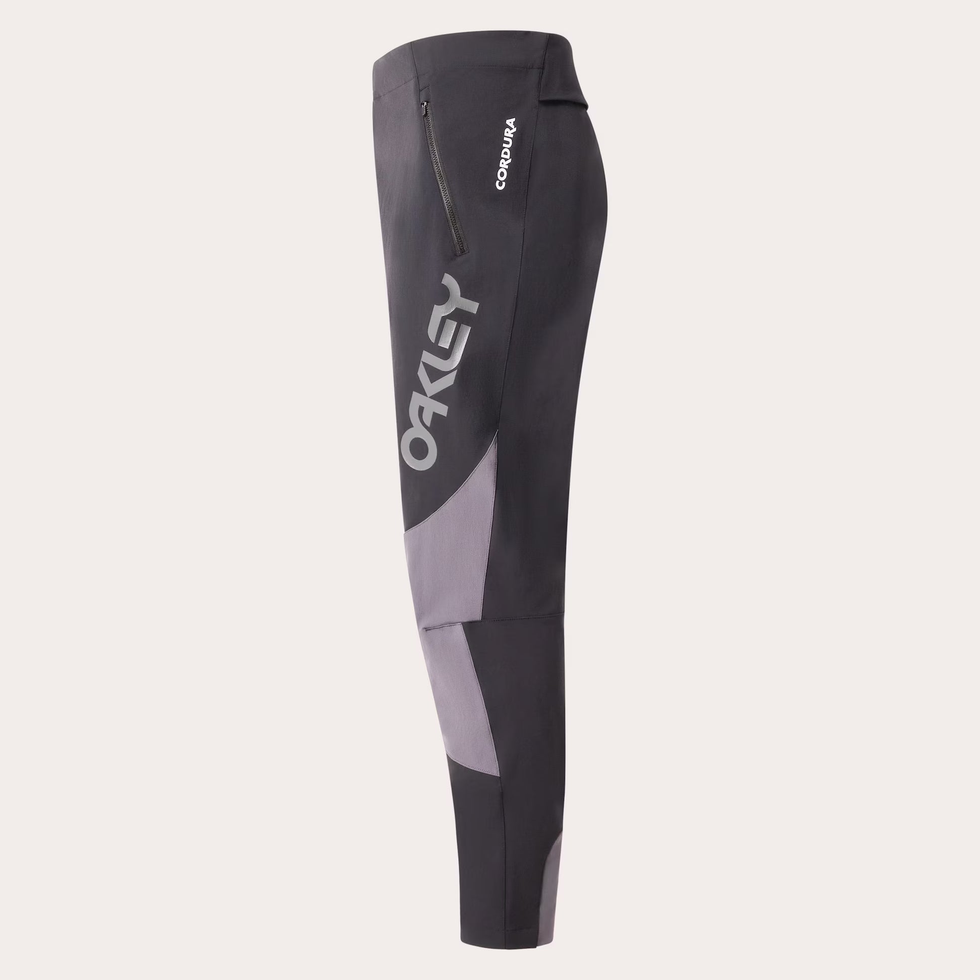 Oakley Cordura cycling tights in dark gray and light gray with a vertical Oakley logo on the side, shown against a light beige background.