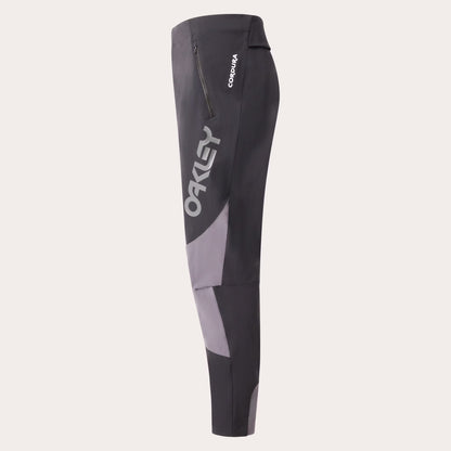 Oakley Cordura cycling tights in dark gray and light gray with a vertical Oakley logo on the side, shown against a light beige background.