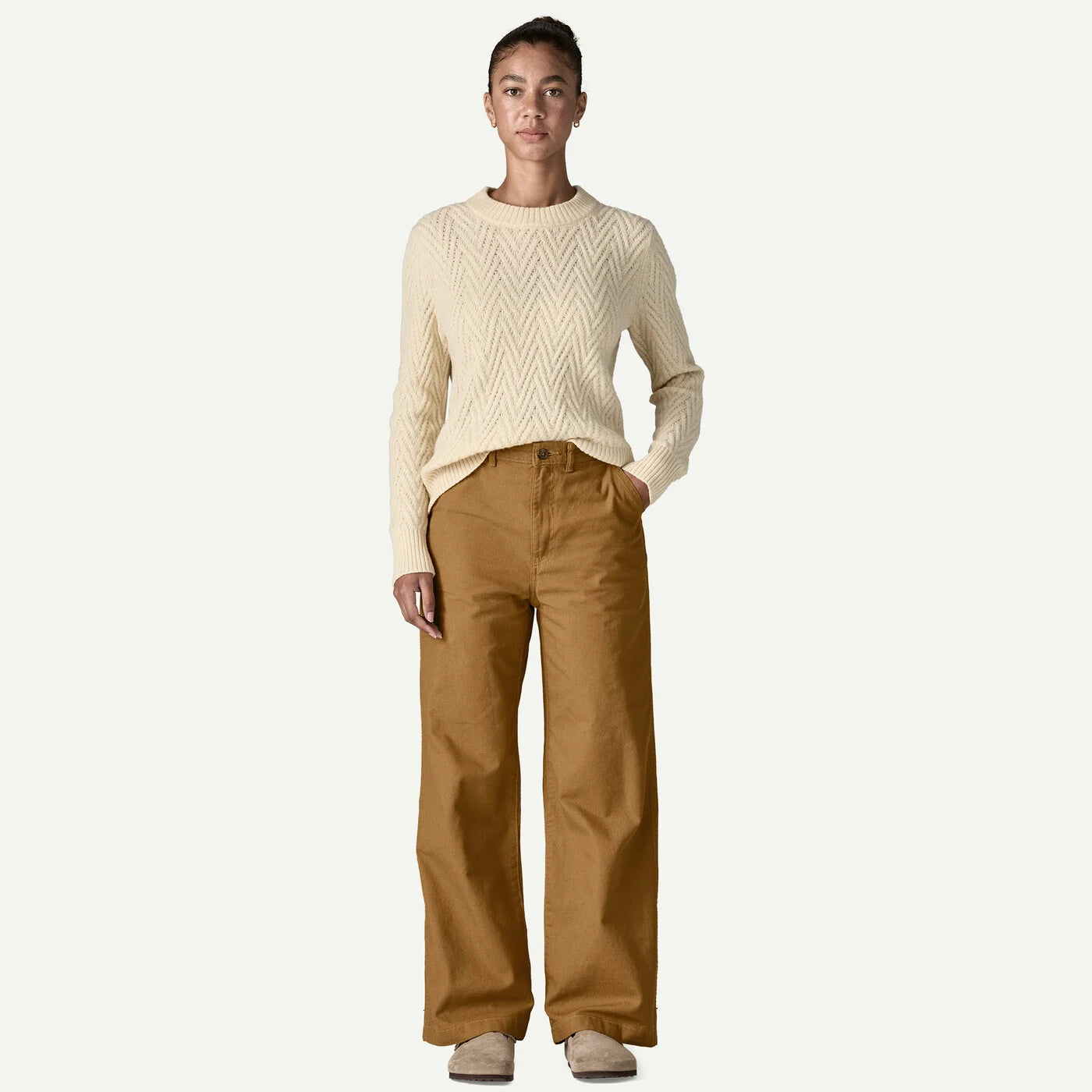 Person wearing a cream sweater and brown pants on a white background