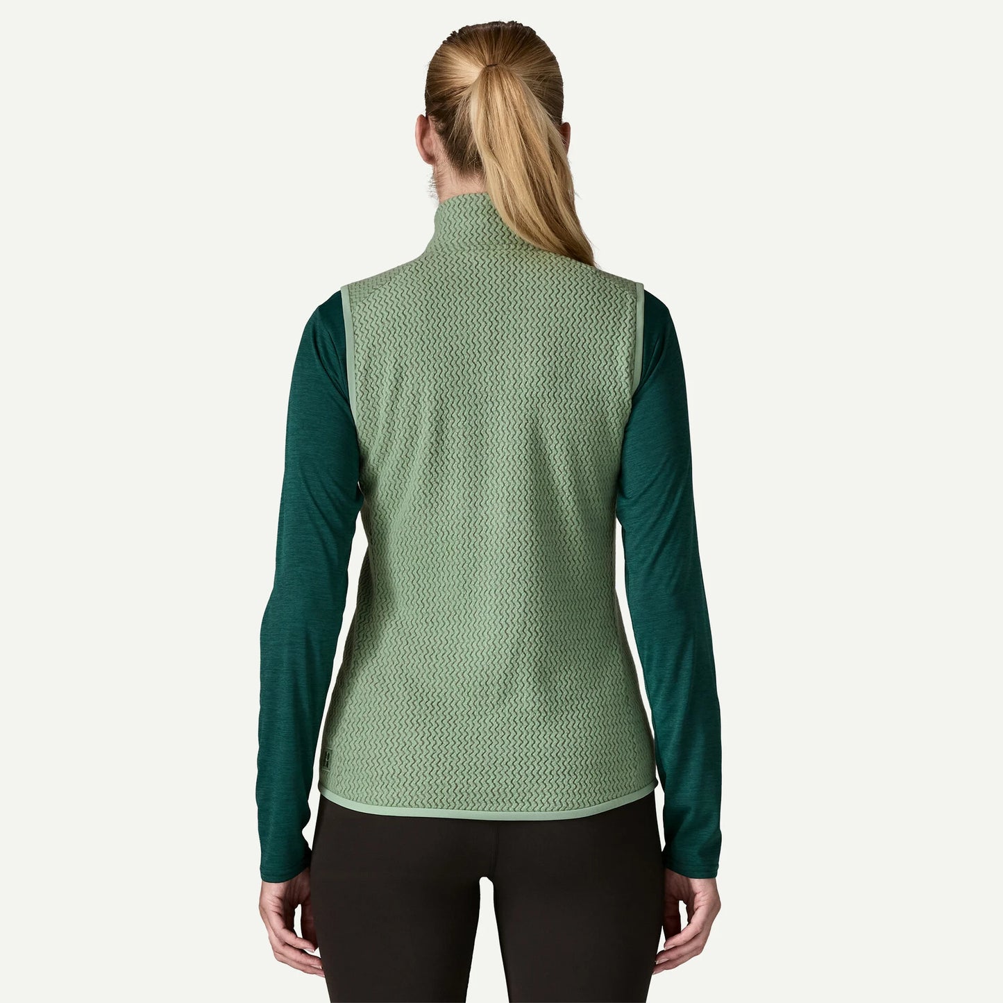 Person wearing a green patterned vest over a long-sleeve shirt on a white background