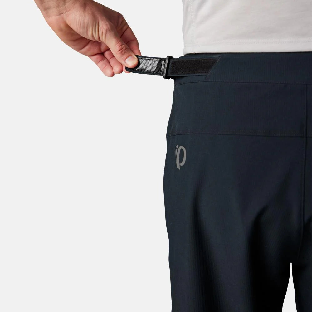 Person adjusting a black belt on navy pants with a brand logo.